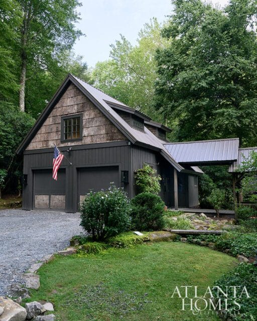 Dark gray garage with wood shingle accents and metal roof, surrounded by trees.