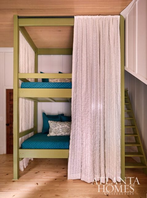Bunk beds with teal bedding and patterned pillows, green frame, white curtains, and wood floors.