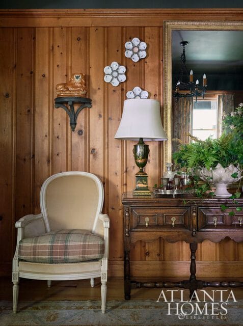 Wood paneled room with upholstered chair, antique desk, and decorative wall art.