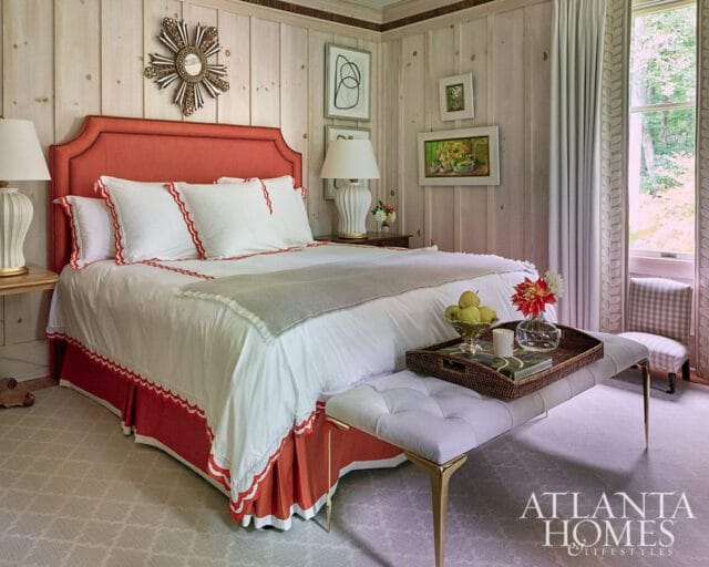 Bedroom with coral headboard, white bedding, wood paneled walls, and a window view
