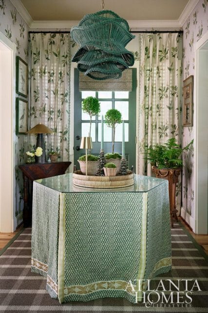 Foyer with green patterned table, wicker chandelier, and botanical print curtains.