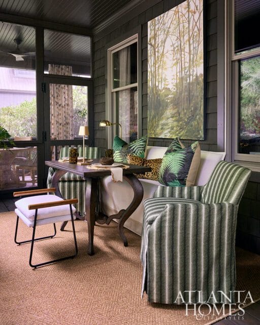 Screened porch with dark wood walls, striped armchair, and botanical art.