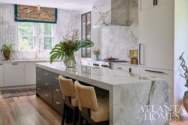 Marble island in modern kitchen with dark wood cabinets and upholstered stools.
