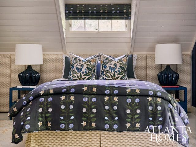 Bedroom with dark floral duvet, patterned headboard, navy lamps, and window with floral shade.