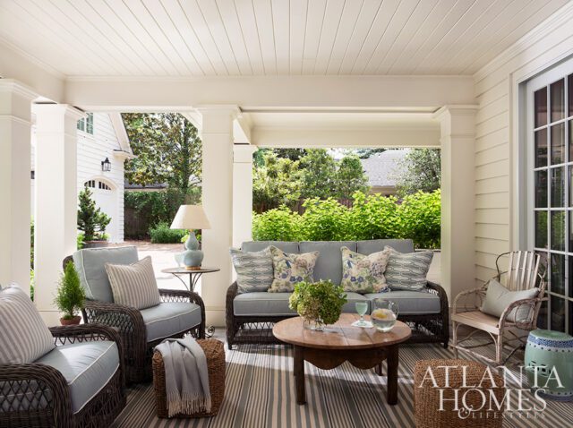 Covered porch with wicker furniture, striped rug, and floral pillows.