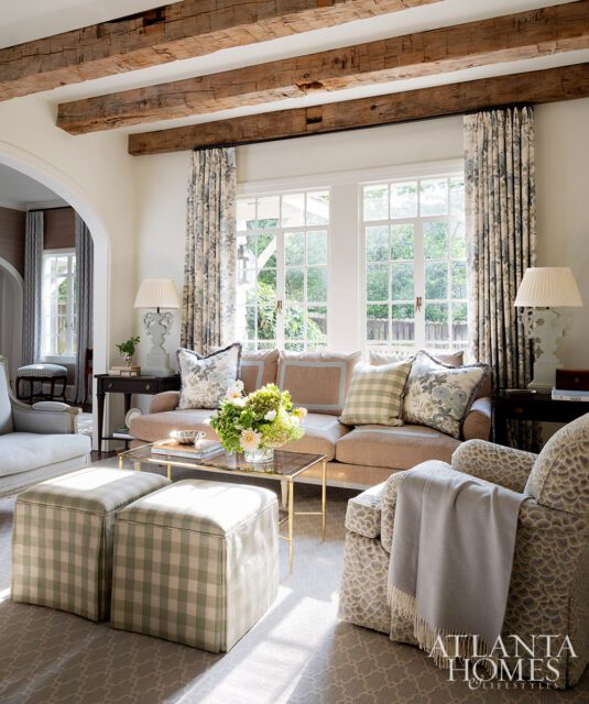 Living room with exposed wood beams, floral curtains, and plaid ottomans.