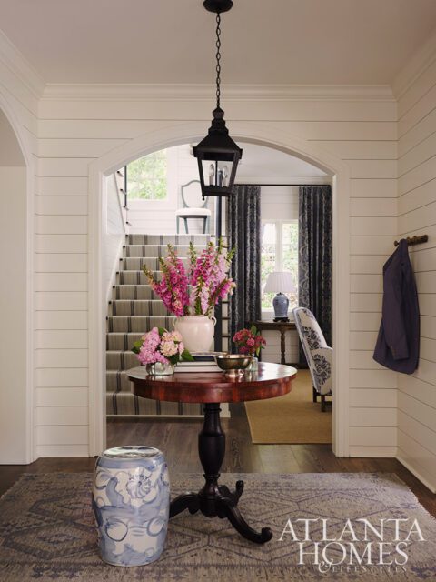 Entryway with shiplap walls, round wood table, floral arrangements, and patterned rug.