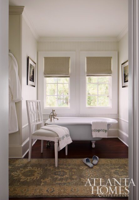 White bathroom with clawfoot tub, beadboard walls, and oriental rug.