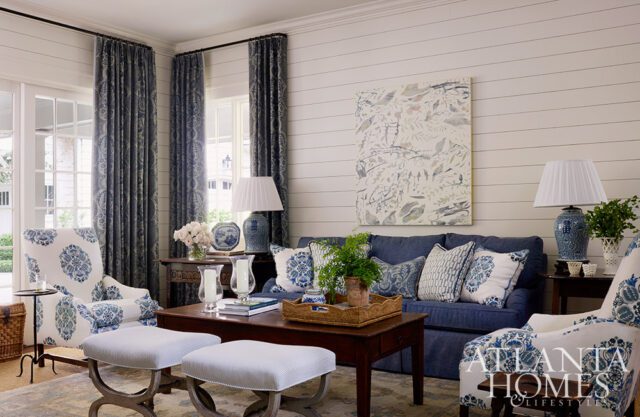 Living room with blue sofa, patterned armchairs, shiplap walls, and botanical art