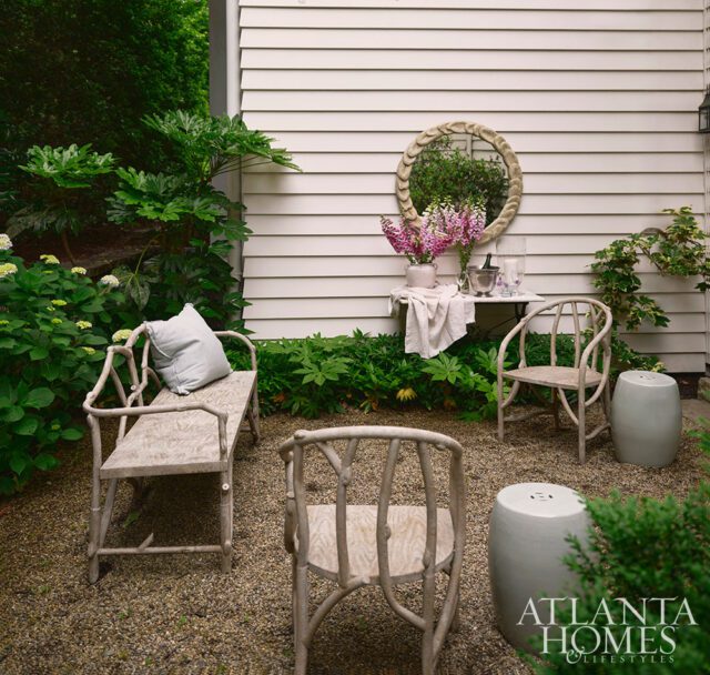 Gravel patio with twig-style chairs, stools, and a table with flowers and mirror.