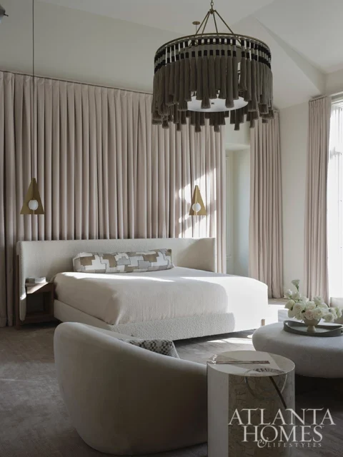 Primary bedroom with bouclé bed, large textured chandelier, and neutral curtains.