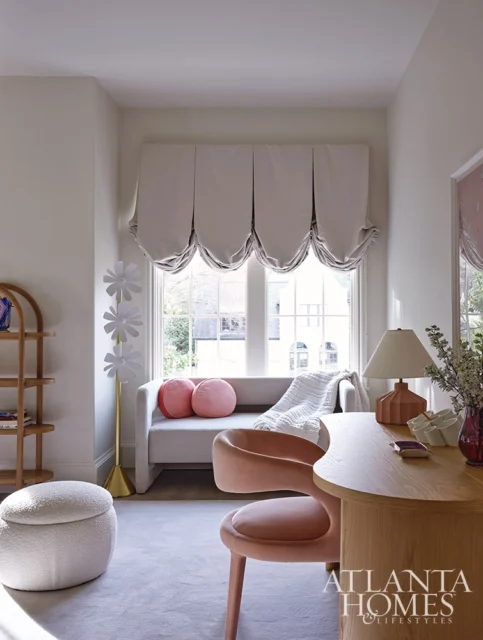Light gray sofa with pink pillows and draped blanket, next to a desk with a pink chair.