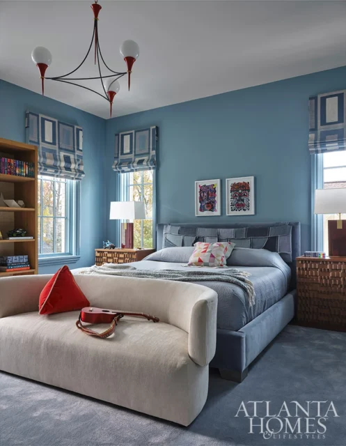 Blue bedroom with upholstered bed, curved sofa, and geometric window treatments.