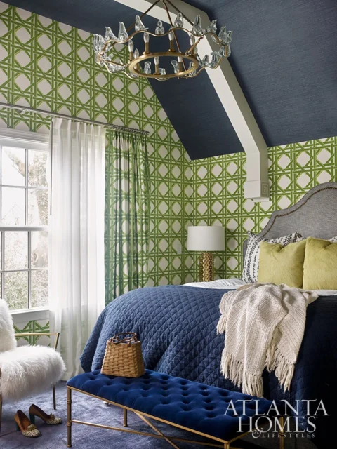 Bedroom with green trellis wallpaper, navy blue bedding, and a tufted blue bench.