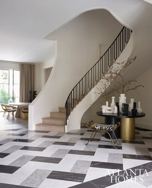 Foyer with curved staircase, geometric marble floor, and console table with vases
