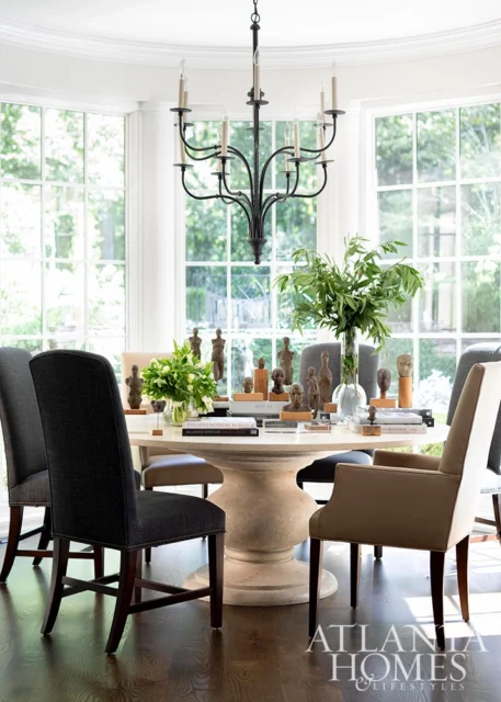 Round dining table with sculptures and greenery, dark wood floor, large windows