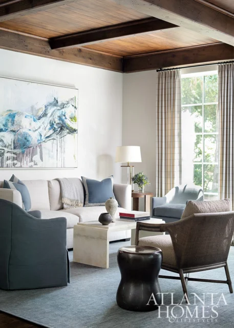 Living room with a white sectional sofa, blue accent chairs, a marble coffee table, and a large abstract painting on the wall.