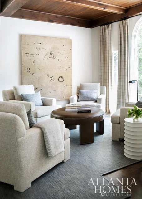 Living room with plush armchairs, leather ottoman coffee table, and large abstract art