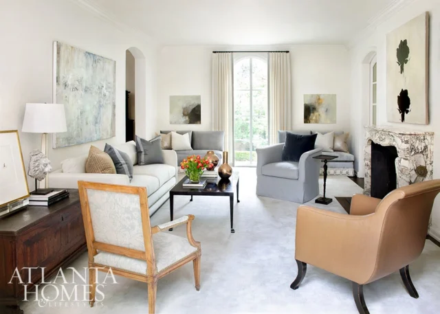 Living room with white sofas, gray armchairs, marble fireplace, and abstract art.