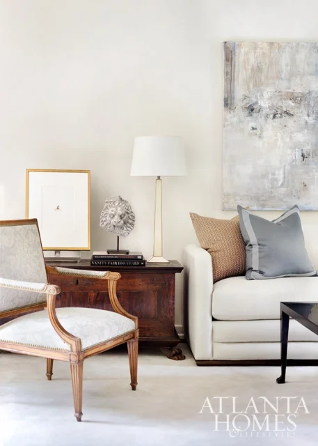 Living room with white sofa, antique wooden chest, framed art, and lion head sculpture.