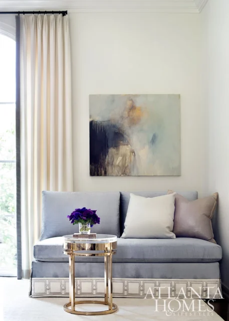 Light blue sofa with pillows, abstract art, and a gold side table with flowers.
