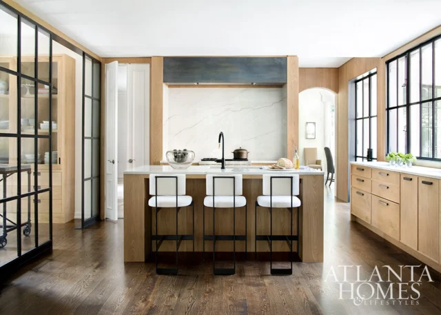 Modern kitchen with light wood cabinetry, marble backsplash, and island with white bar stools.
