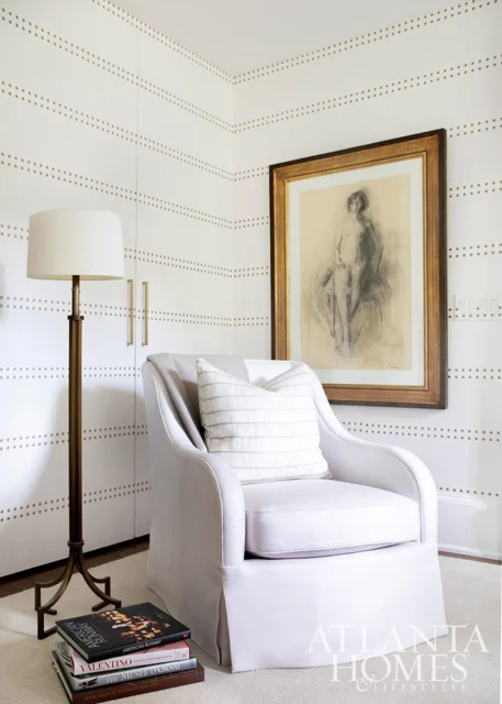 White armchair with striped pillow next to a floor lamp and framed art