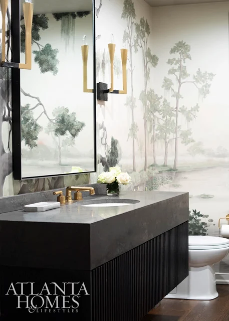 Powder room with dark vanity, concrete countertop, brass fixtures, and scenic wallpaper.