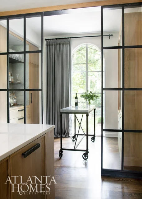 Kitchen with wood cabinetry, marble island, and black-framed glass doors.