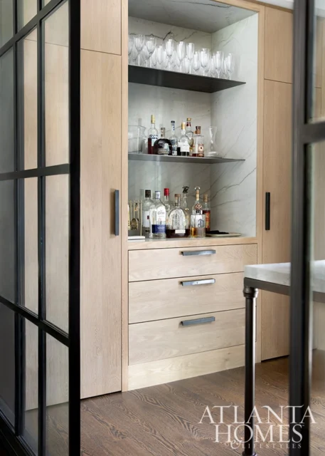 Built-in bar with light wood cabinetry, marble backsplash, and shelves stocked with glassware and