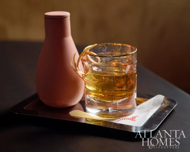 Cocktail with orange peel garnish and a terracotta carafe on a silver tray.
