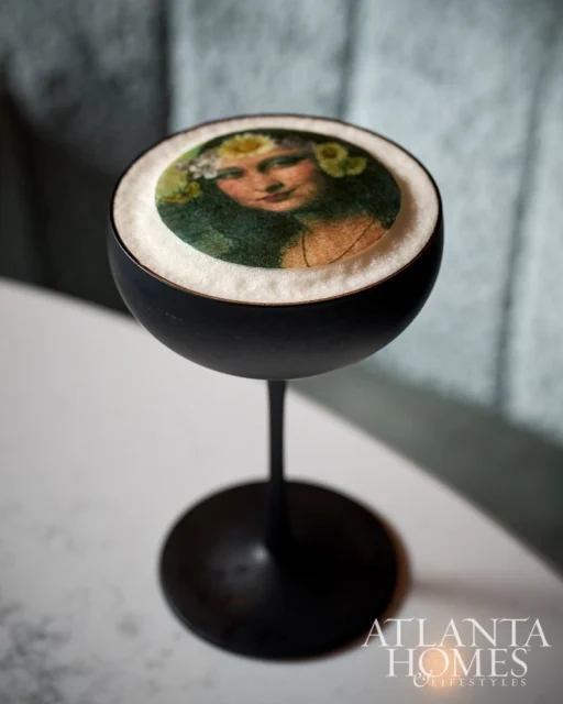 Cocktail with foam art of a woman wearing a flower crown and the Atlanta Homes & Lifestyles logo.