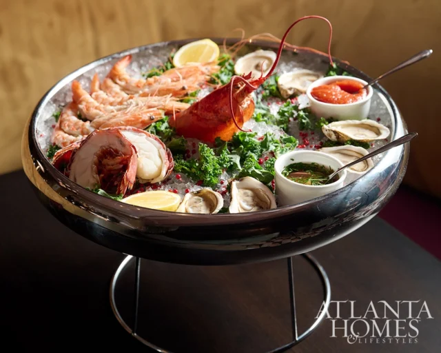 Seafood platter with lobster, shrimp, oysters, and dipping sauces on ice.