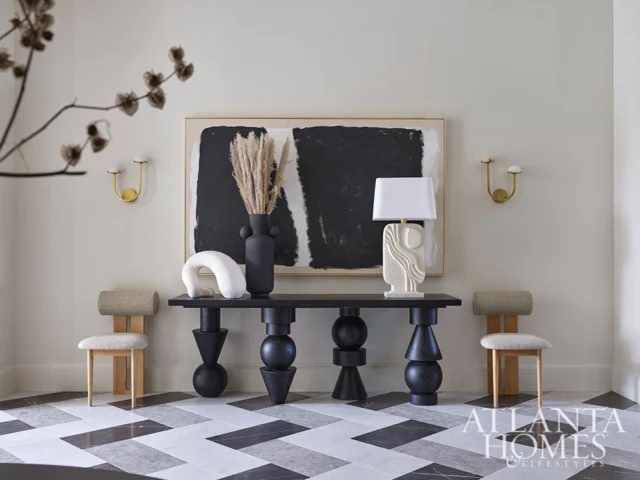 Foyer with black console table, abstract art, and two chairs on geometric floor.
