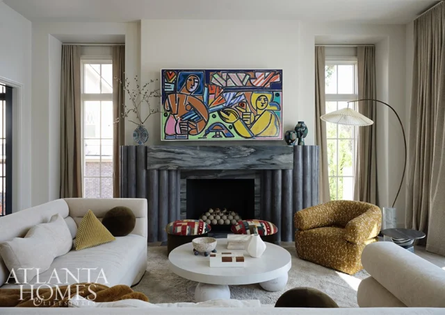 Living room with abstract art above a fluted fireplace, cream sectional, and yellow armchair.