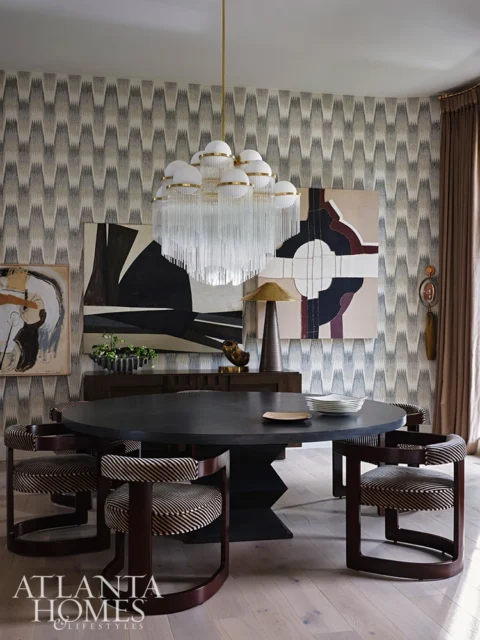 Dining room with patterned wallpaper, round black table, striped chairs, and glass chandelier.
