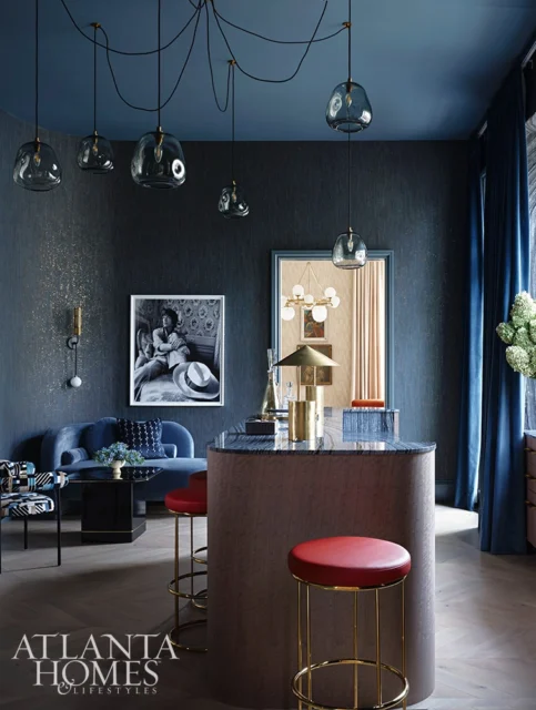 Dark blue room with curved island, red bar stools, blue sofa, and glass pendant lights.