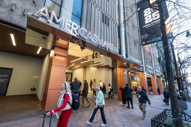 AmericasMart building entrance with neon sign, people walking on sidewalk.