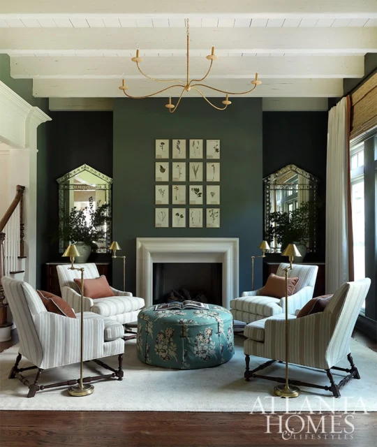 Living room with striped armchairs, floral ottoman, fireplace, and botanical prints