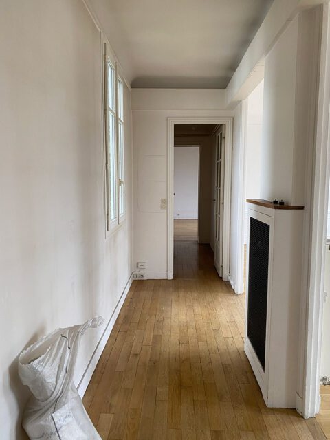 Hallway with hardwood floors, white walls, and a window. A white bag sits by the wall.