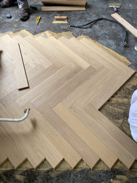 Light oak hardwood flooring laid in a herringbone pattern during installation