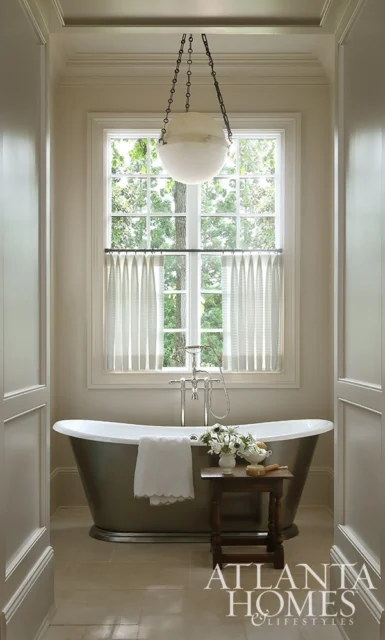 Bathroom with freestanding tub, window with sheer curtains, and hanging globe light.