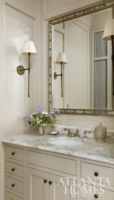 Powder room with marble vanity, brass fixtures, and sconce lighting.