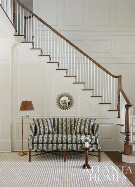Sofa with green and white striped upholstery in front of a white paneled staircase