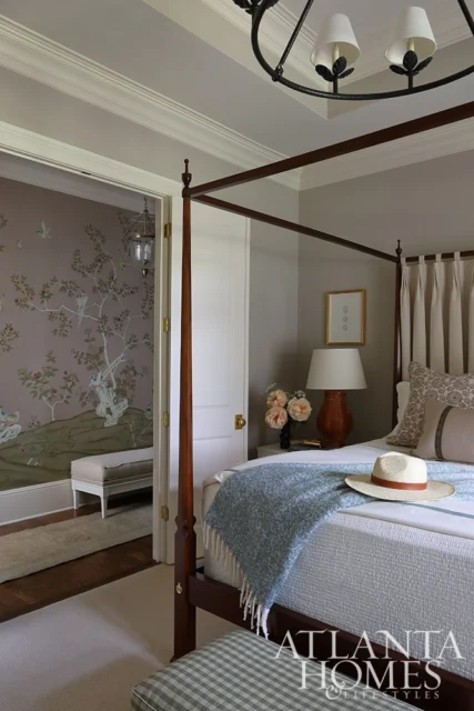 Bedroom with four-poster bed, blue throw, and chinoiserie wallpaper visible through doorway.