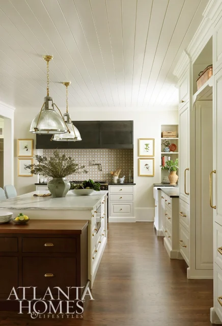 White kitchen with marble island, brass hardware, and dark wood cabinetry.