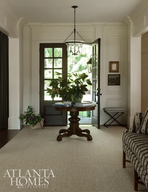 Entryway with dark wood door, round pedestal table with plant, and striped sofa.