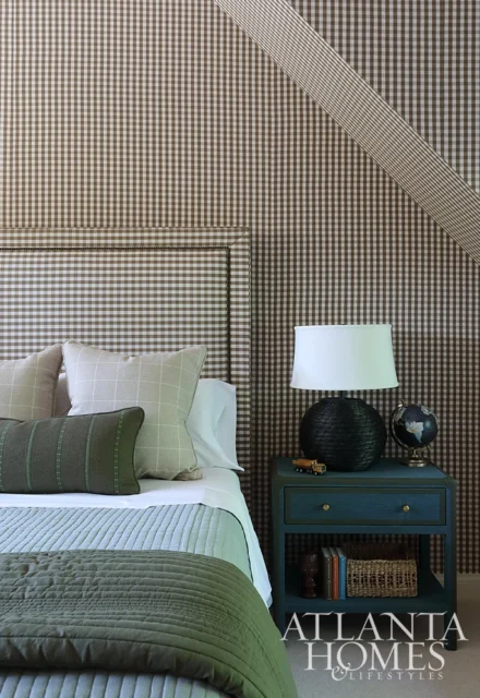 Bedroom with brown gingham wallpaper, upholstered headboard, and blue nightstand with lamp and