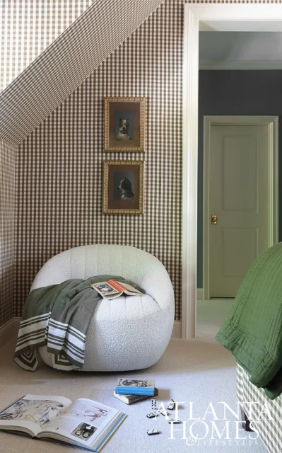 Bedroom with brown gingham wallpaper, white boucle chair, and green throw