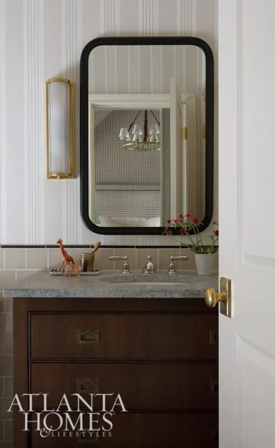 Dark wood vanity with stone countertop, striped wallpaper, and brass sconce.